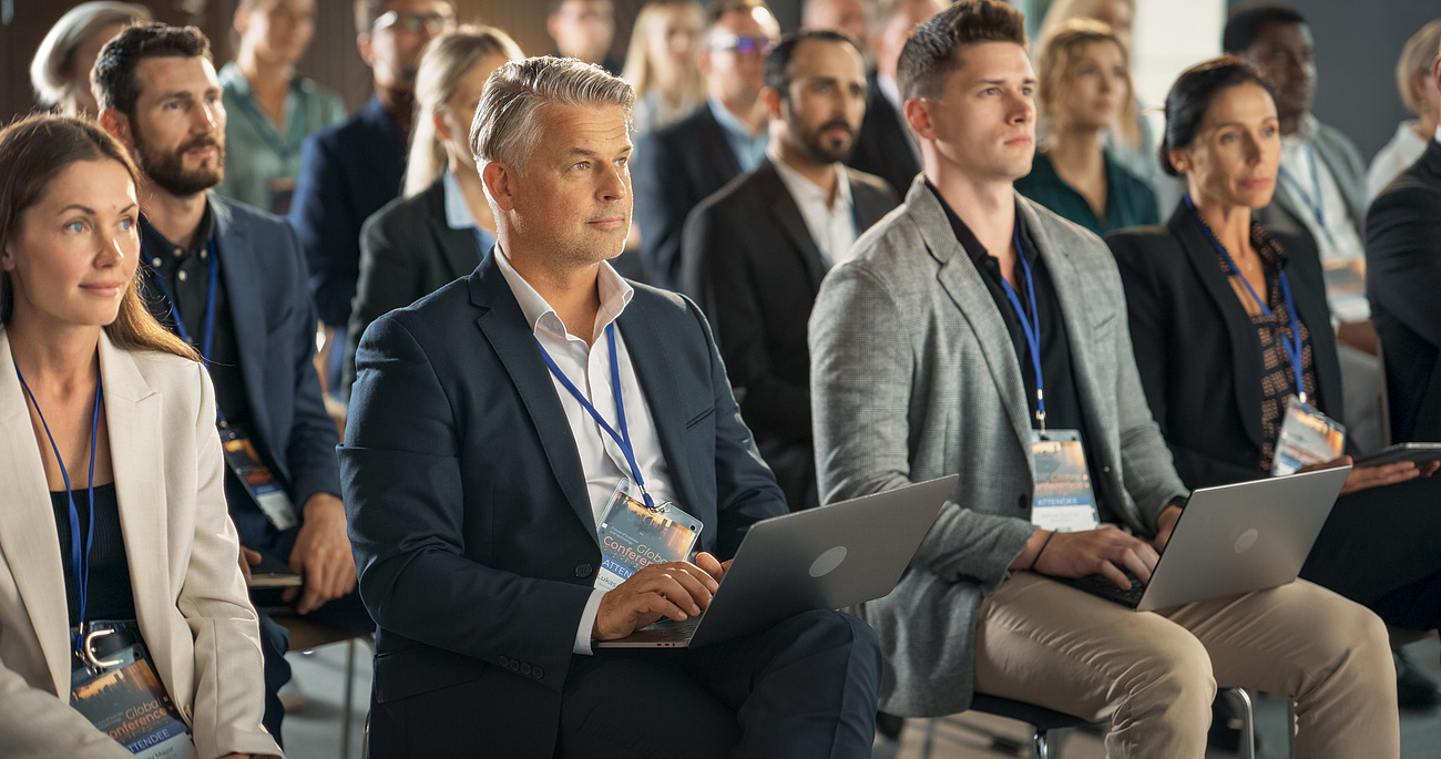 Aufmerksame Teilnehmende in der ersten Reihe des Publikums einer Konferenz Aufmerksame Teilnehmende in der ersten Reihe des Publikums einer Konferenz